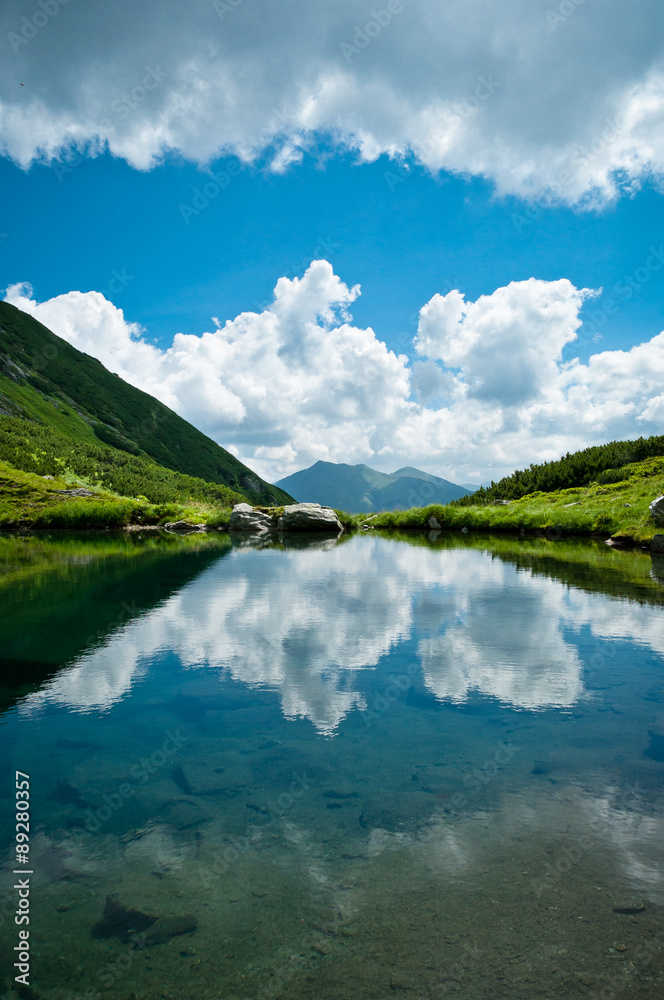 View of a lake, with clouds and blue sky reflected in it.