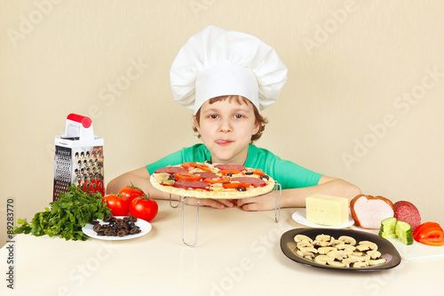 Little funny chef appetizing licked near the cooked pizza