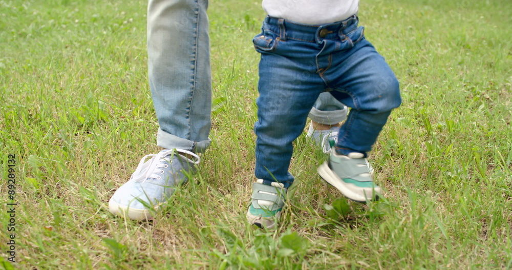 Legs of baby boy walking on grass helped by his father Legs of baby boy walking on grass helped by his father