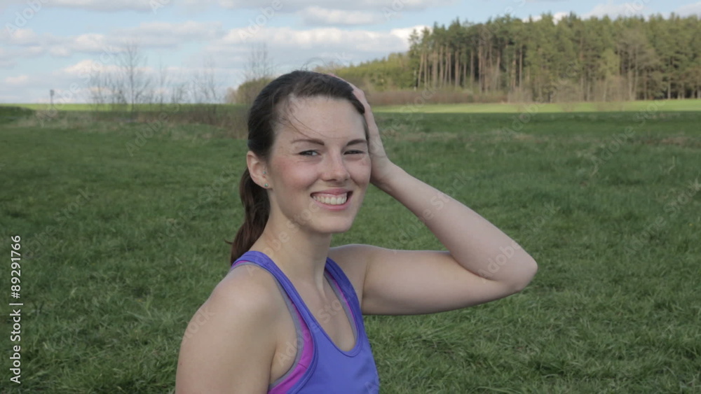 young woman in sports gear standing outdoors in the grass and smiling at camera young woman in sports gear standing outdoors in the grass and smiling at camera