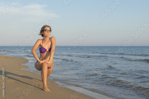 Girl in bikini stretching and exercising at the beach