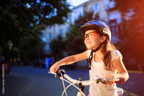 little girl with bicycle in summer park against sunset