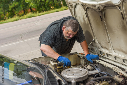 Senior man doing own car repair on the road