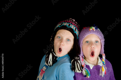 two girls in winter caps singing with black background