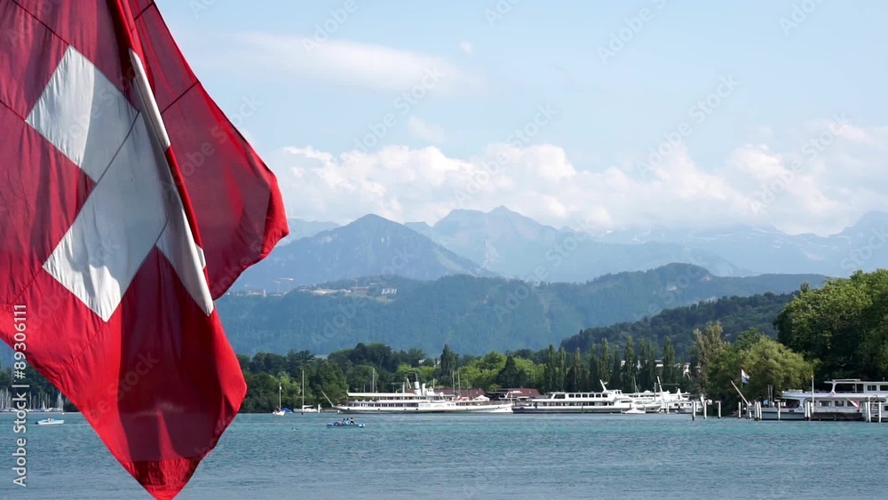 Panorama view the of lake lucerne in switzerland with huge swiss flag waving in the foreground.