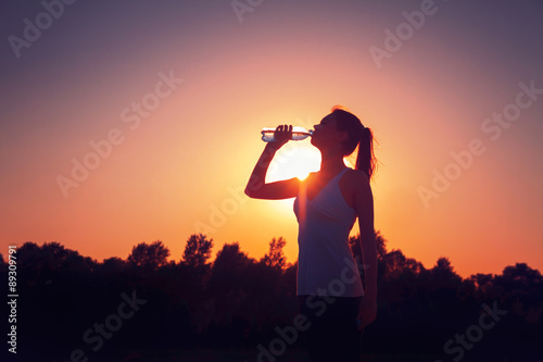 Silhouette of a girl at sunset with a bottle of water