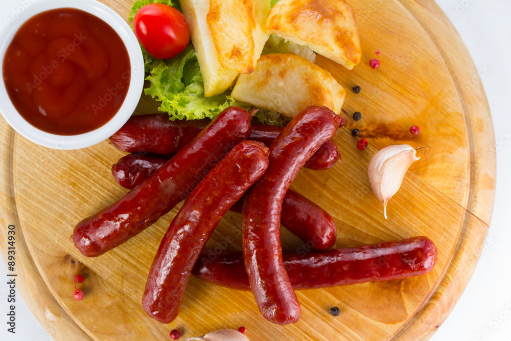 Tasty grilled sausages with vegetables and sauce close up on wooden board isolated on white background Tasty grilled sausages with vegetables and sauce close up on wooden board isolated on white background