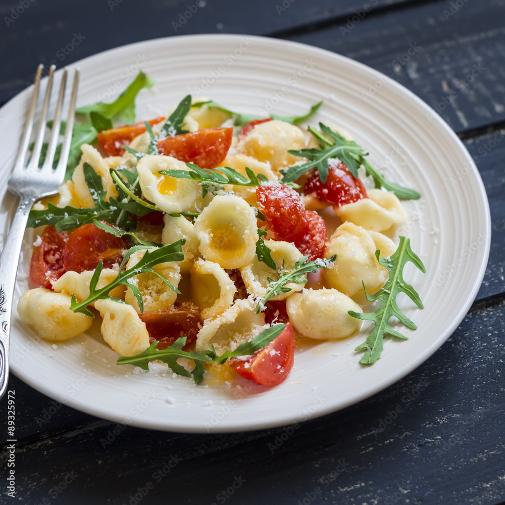 orecchiette pasta with tomatoes, Parmesan and rocket salad on a plate light on a dark wooden background orecchiette pasta with tomatoes, Parmesan and rocket salad on a plate light on a dark wooden background
