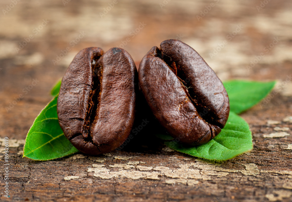 Obraz premium Coffee grains and green leaf on grunge wooden background