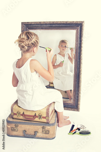 Child or young girl putting on make-up while looking at herself photo