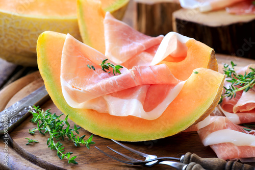 Prosciutto with melon or rustic wooden background