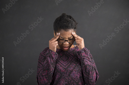 African woman with fingers on temples thinking on blackboard background