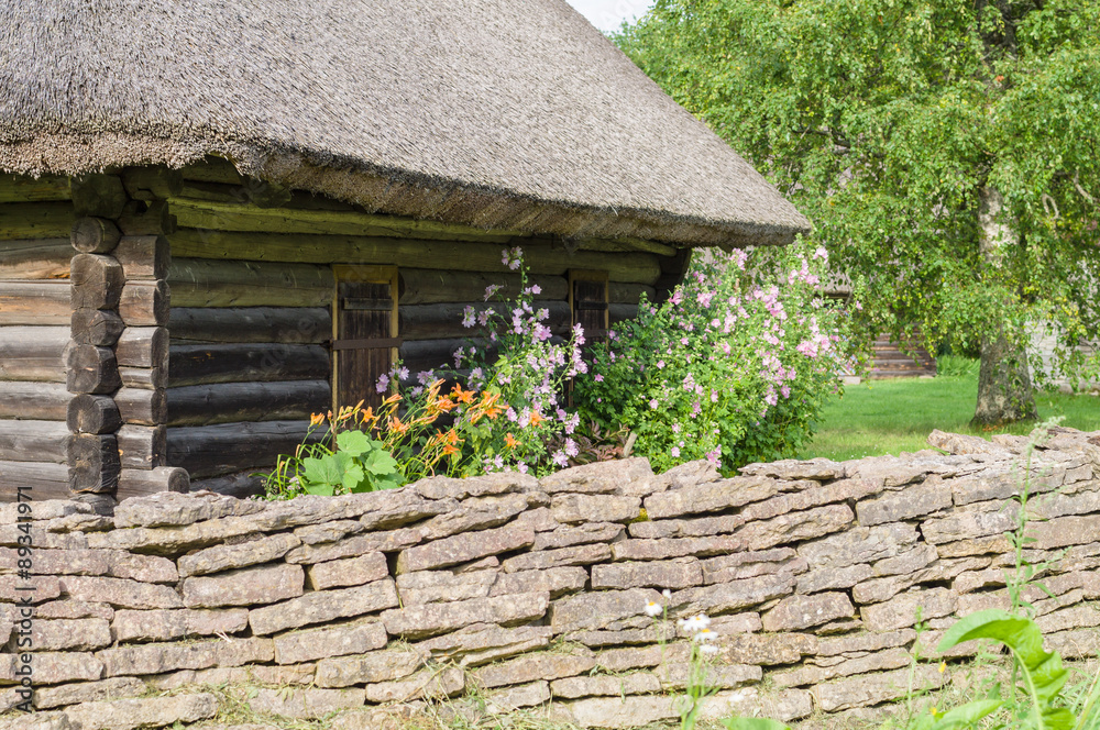 Rural log cabin with garden flowers and limestone fence on foreground Rural log cabin with garden flowers and limestone fence on foreground