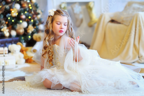 Christmas time, adorable girl in fancy dress sitting in the Christmas decorated interior and holding pearl beads © Zoja