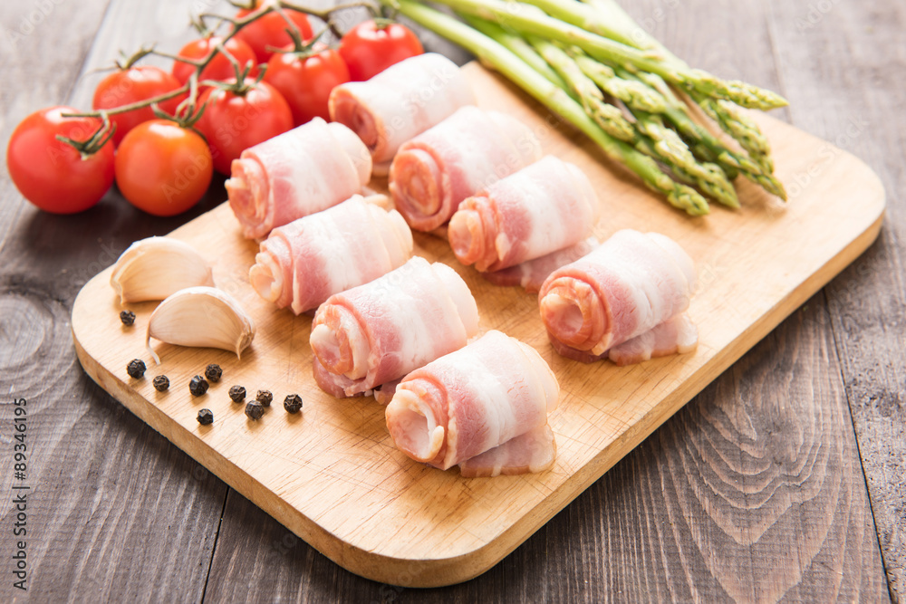 Bacon rolls with tomato, garlic, asparagus on wooden background Bacon rolls with tomato, garlic, asparagus on wooden background