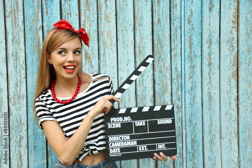 Obraz premium Beautiful girl with pretty smile holding clapboard on color wooden background