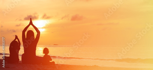 silhouette of mother and kids doing yoga at sunset sea