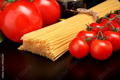 Long pasta raw isolated on black with tomatoes and olive oil