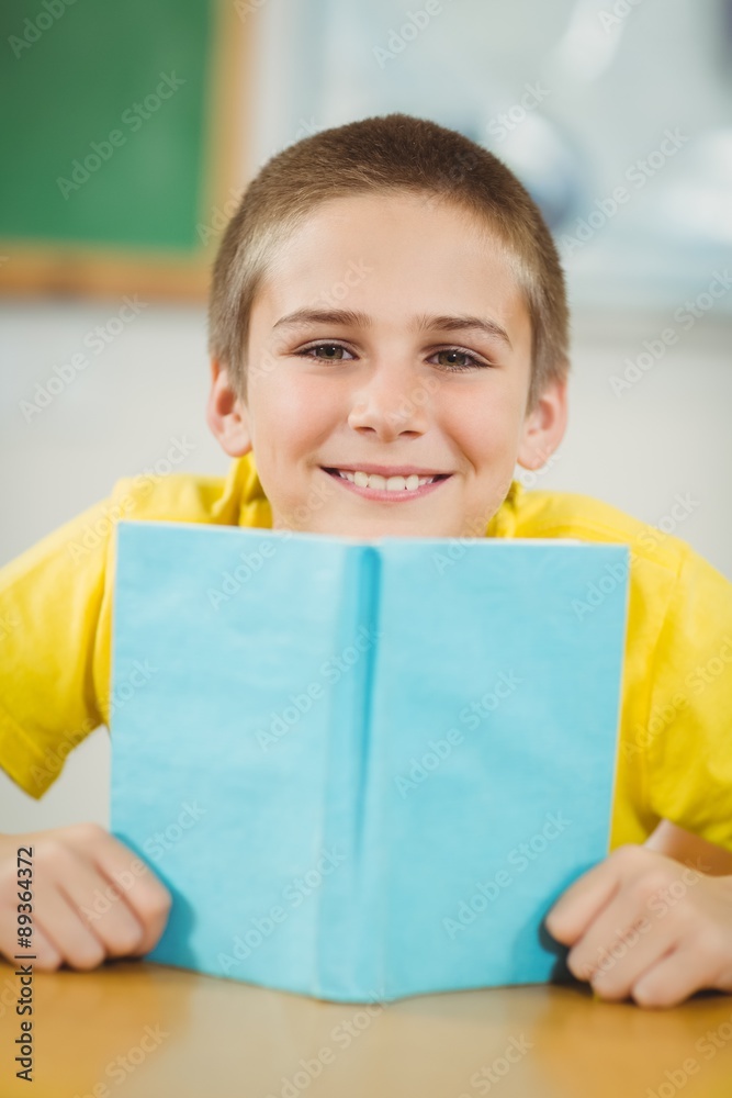 Smiling pupil reading book in a classroom Smiling pupil reading book in a classroom