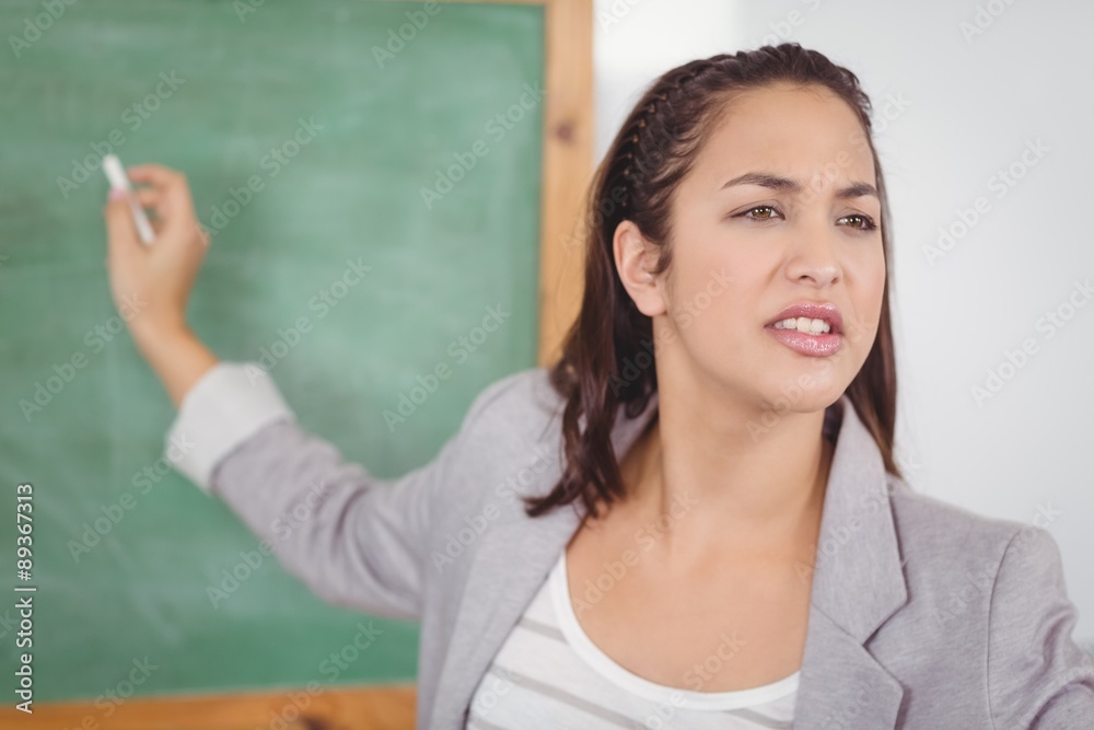 Pretty teacher writing on chalkboard in a classroom Pretty teacher writing on chalkboard in a classroom