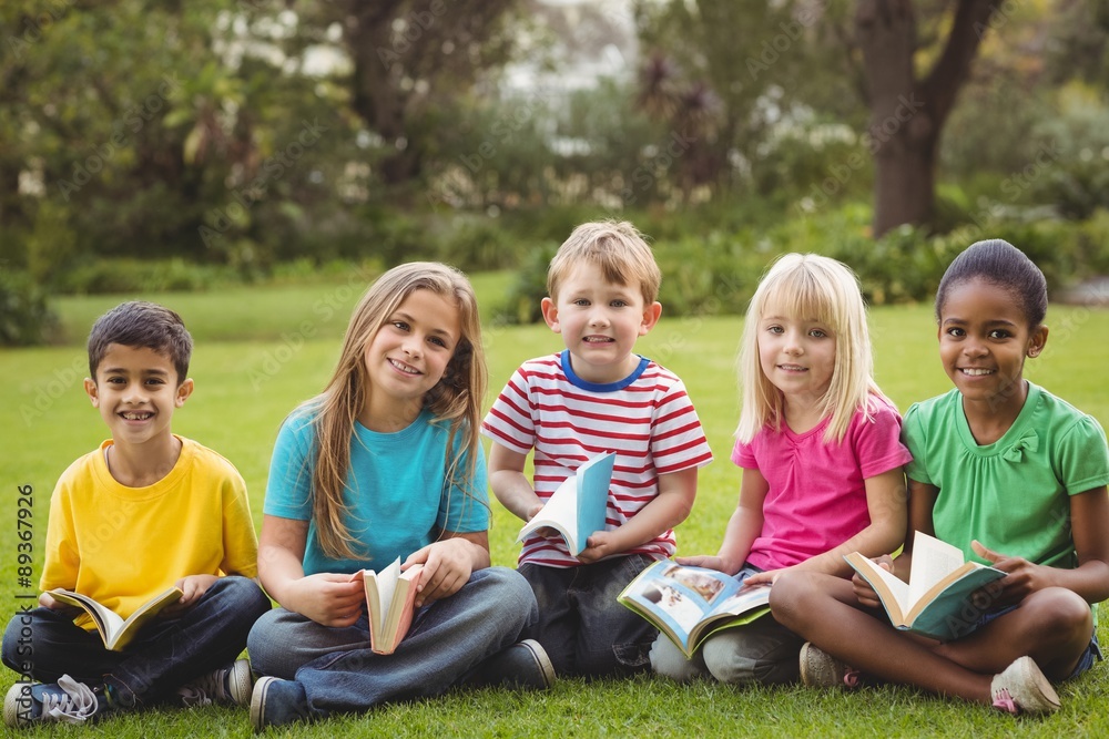 Smiling classmates sitting in grass and holding books
