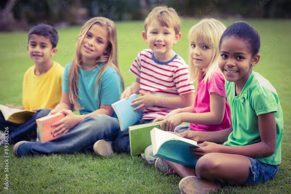 Smiling classmates sitting in grass and holding books Smiling classmates sitting in grass and holding books