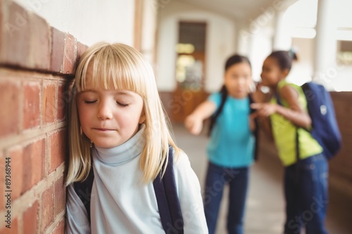Sad pupil being bullied by classmates at corridor