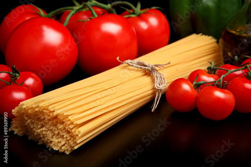 Long pasta raw isolated on black with tomatoes and olive oil