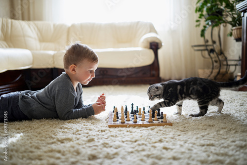 little boy plays chess lying on floor