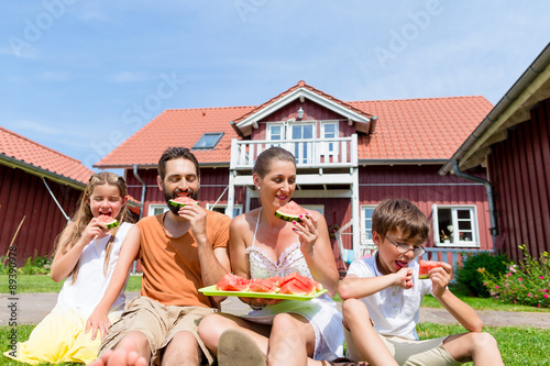 Family sitting in grass front of home eating water melon