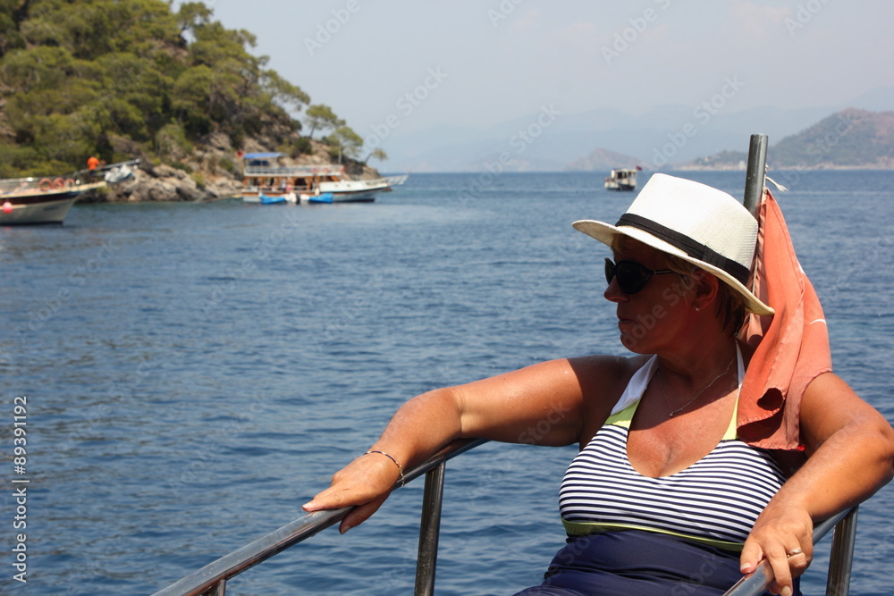 A mature woman wearing sunglasses and a hat  while on a boat trip during a vacation in turkey