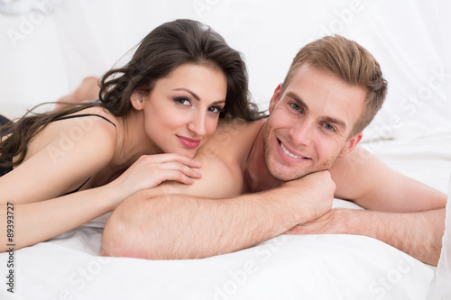Happy young couple lying in white bed,
