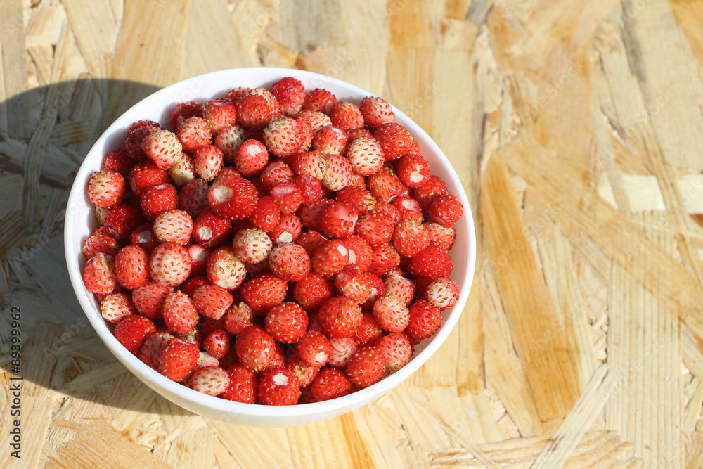 Ripe red wild strawberry in a plate on a wooden table outdoors Ripe red wild strawberry in a plate on a wooden table outdoors