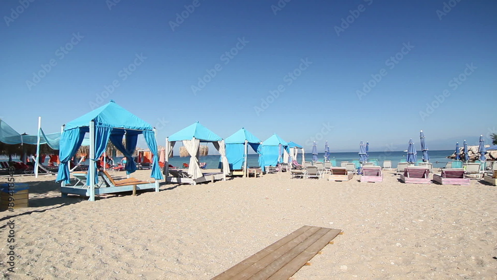 Relaxing summer morning scene with blue beach gazebos and parasols on fine light sand by the sea Relaxing summer morning scene with blue beach gazebos and parasols on fine light sand by the sea