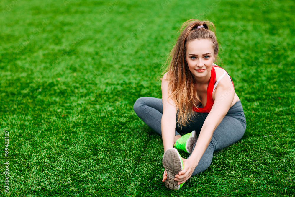Young fitness girl sitting on green grass . Young fitness girl sitting on green grass .