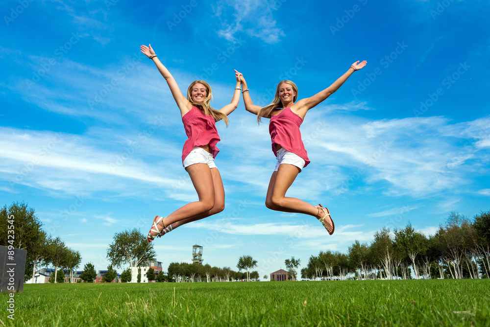 two young women jumping in the air holding hands in unison two young women jumping in the air holding hands in unison