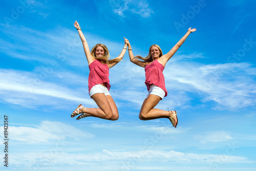 two pretty girls jumping in park holding hands