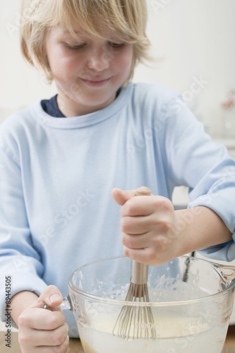 Boy stirring baking mixture in glass bowl with whisk photo