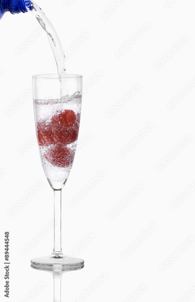 Pouring water into glass containing raspberries