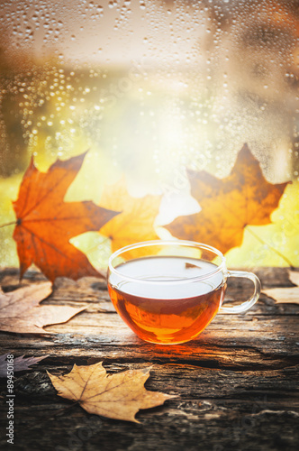 cup of tea with autumn leaves on wooden window sill, with autumn nature background