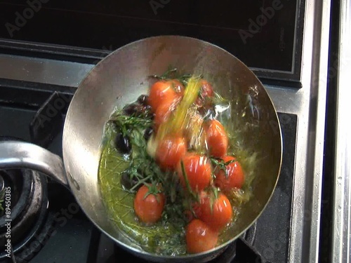 Frying tomatoes, garlic, olives and herbs photo