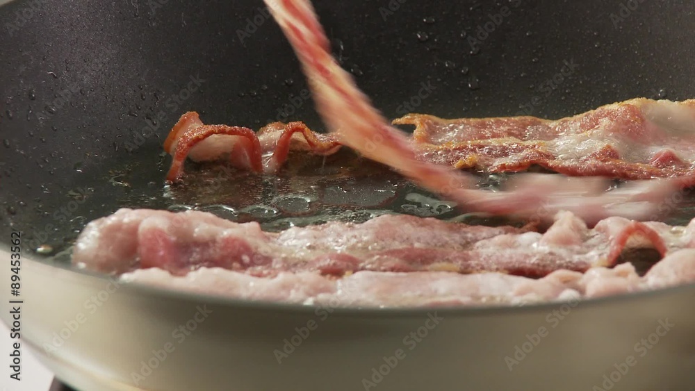 Rashers of bacon being fried and turned in a pan