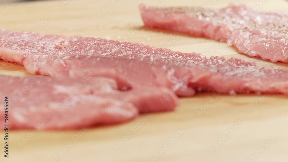 Tenderised veal escalopes being turned and seasoned with salt and pepper Tenderised veal escalopes being turned and seasoned with salt and pepper