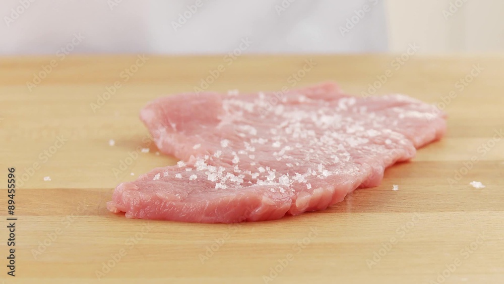 Tenderised veal escalopes being seasoned on both sides with salt and pepper Tenderised veal escalopes being seasoned on both sides with salt and pepper