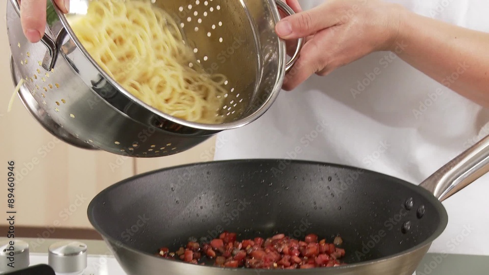 Spaghetti being added to fried bacon