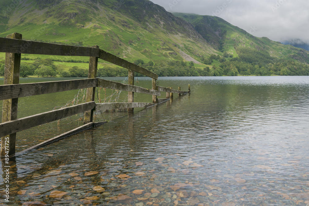 Wooden fence merges into Buttermere Lake, Lake District National Park, Cumbria England.