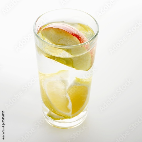 A glass of water with lemon and apple wedges