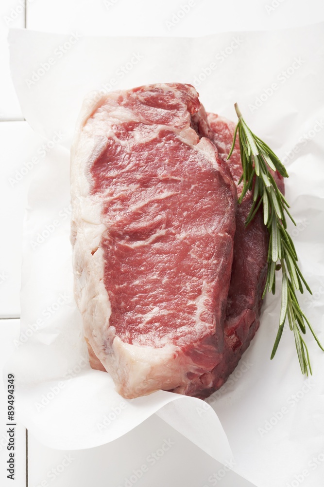 Two slice of entrecôte with rosemary on parchment paper