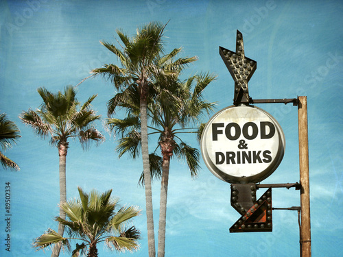 aged and worn vintage food and drinks sign on beach with palm trees