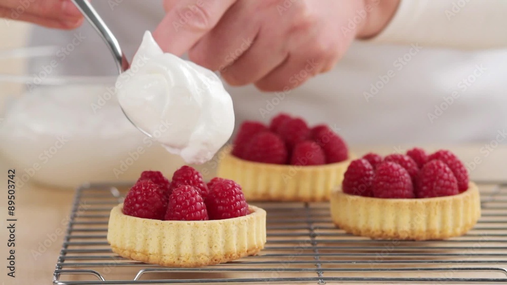 Meringue being spread onto raspberry tartlets Meringue being spread onto raspberry tartlets